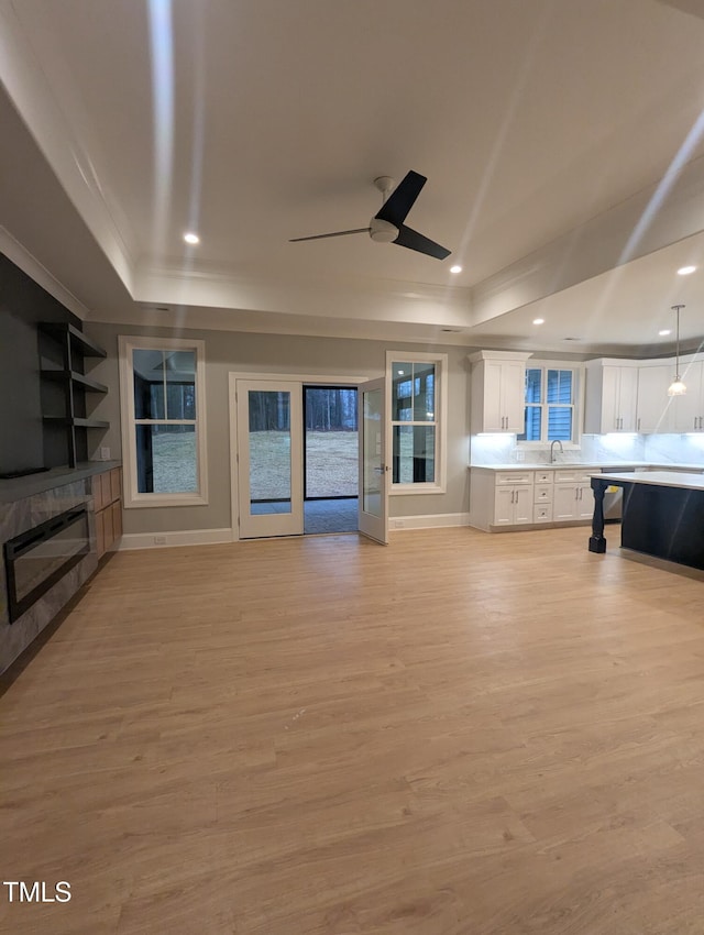 unfurnished living room with light hardwood / wood-style flooring, crown molding, ceiling fan, and a raised ceiling