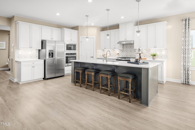 kitchen featuring stainless steel appliances, sink, pendant lighting, white cabinetry, and an island with sink