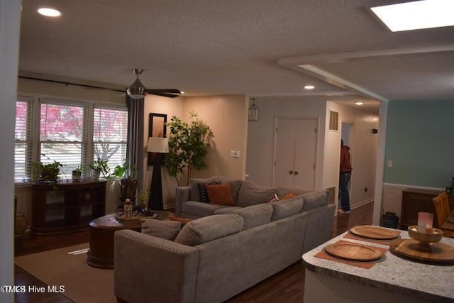 living room featuring ceiling fan, a skylight, dark wood-type flooring, and a textured ceiling