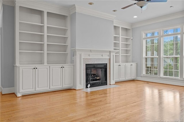 unfurnished living room with built in shelves, crown molding, ceiling fan, and light wood-type flooring