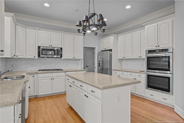 kitchen with sink, a kitchen island, decorative light fixtures, white cabinets, and appliances with stainless steel finishes