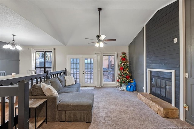 living room featuring carpet flooring, a fireplace, ceiling fan with notable chandelier, and vaulted ceiling