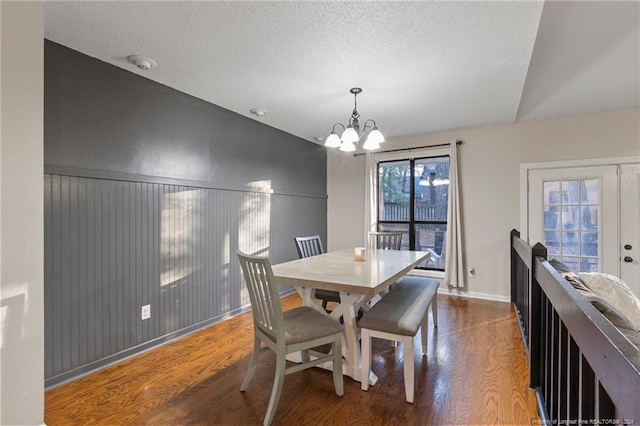 dining room with hardwood / wood-style floors, a notable chandelier, lofted ceiling, and a textured ceiling