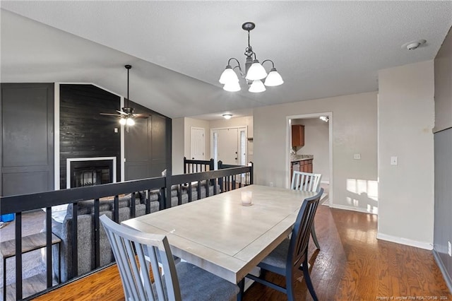 dining space featuring ceiling fan with notable chandelier, a large fireplace, dark wood-type flooring, and lofted ceiling