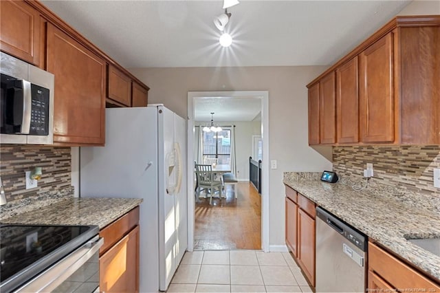 kitchen featuring decorative backsplash, appliances with stainless steel finishes, light stone counters, a notable chandelier, and light hardwood / wood-style floors