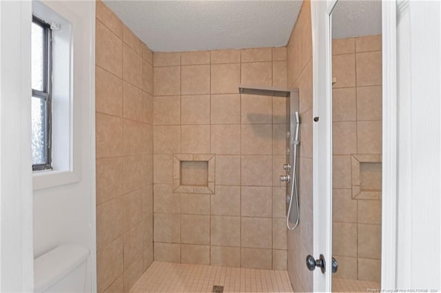 bathroom with tiled shower, a textured ceiling, toilet, and a healthy amount of sunlight