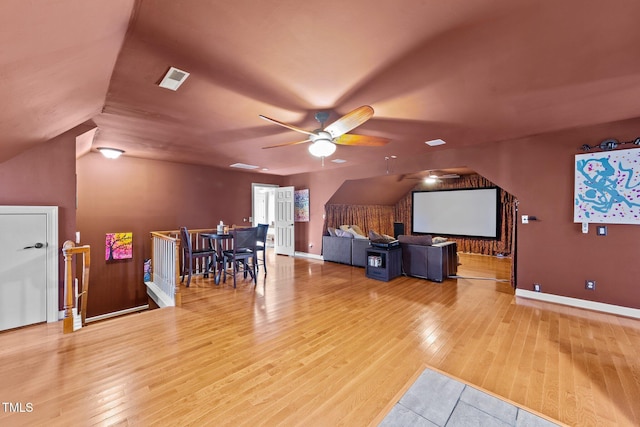 home theater room featuring ceiling fan, light wood-type flooring, and vaulted ceiling