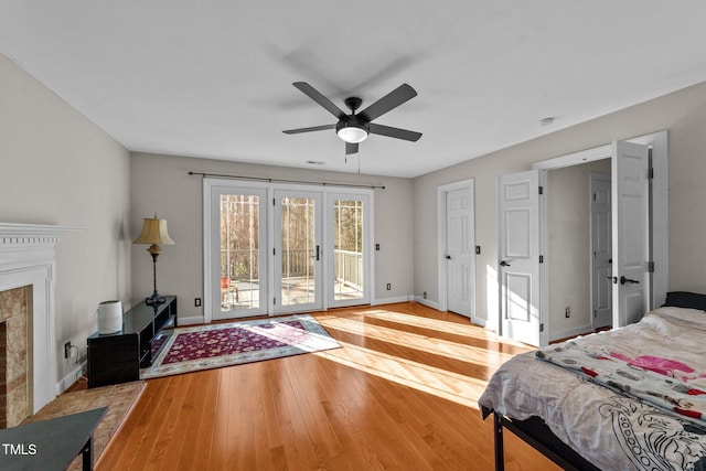 bedroom featuring french doors, access to exterior, ceiling fan, light hardwood / wood-style floors, and a brick fireplace