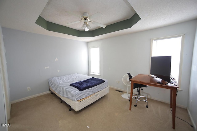 carpeted bedroom with a tray ceiling, ceiling fan, and a textured ceiling