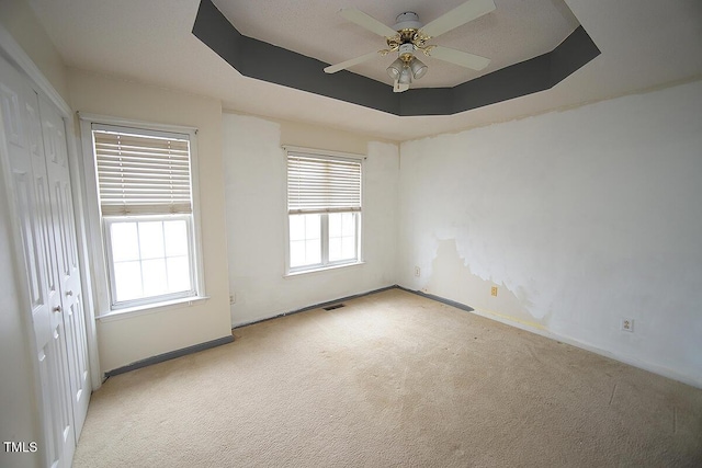 spare room featuring light colored carpet, a raised ceiling, and ceiling fan