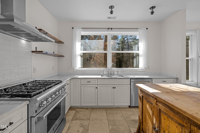 kitchen featuring appliances with stainless steel finishes, tasteful backsplash, wall chimney exhaust hood, sink, and white cabinets