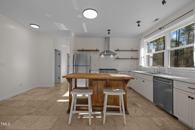 kitchen featuring a breakfast bar, backsplash, wall chimney range hood, appliances with stainless steel finishes, and white cabinetry