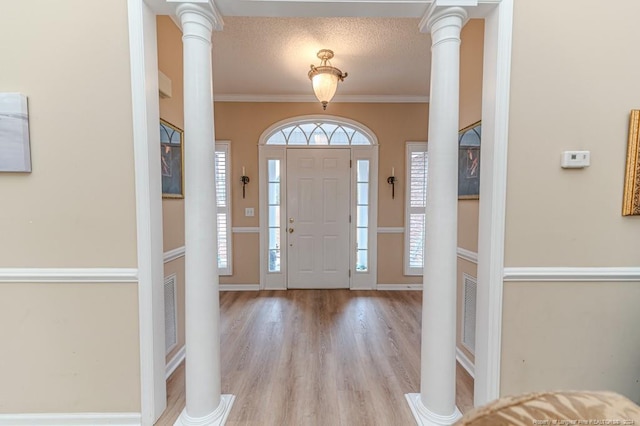 foyer entrance with a textured ceiling, light hardwood / wood-style floors, ornate columns, and crown molding