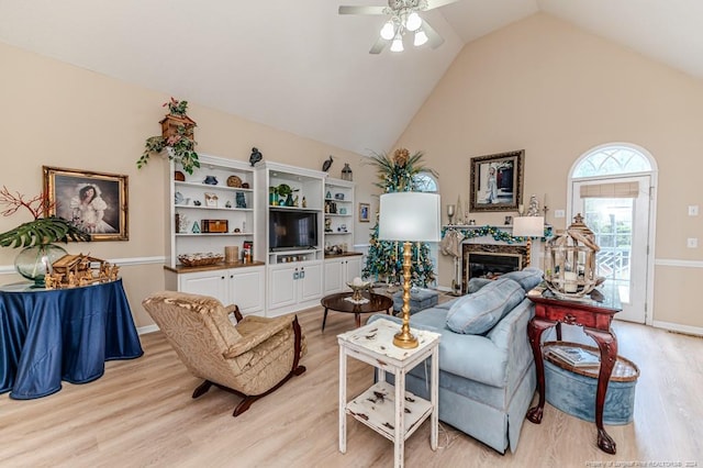 living room with a high end fireplace, light wood-type flooring, high vaulted ceiling, and ceiling fan