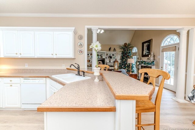 kitchen with white dishwasher, white cabinetry, sink, and decorative columns