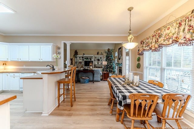 dining area with light wood-type flooring, ornate columns, crown molding, and sink