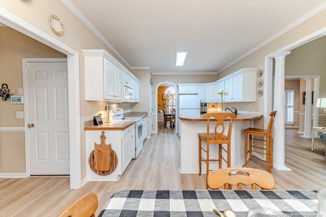 kitchen featuring kitchen peninsula, decorative columns, white appliances, light hardwood / wood-style flooring, and white cabinets