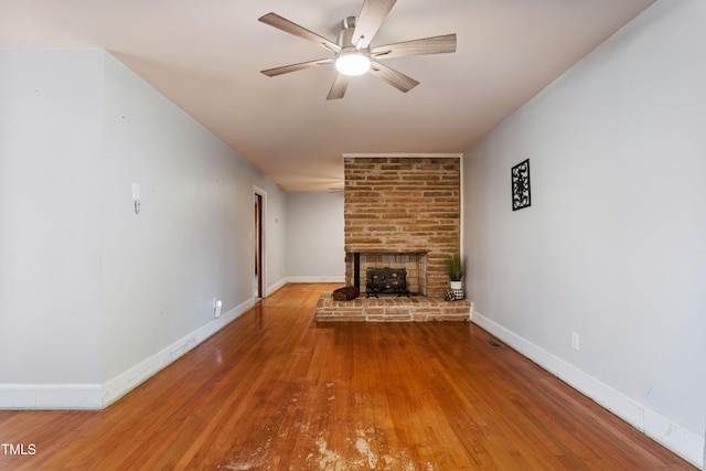 unfurnished living room featuring wood-type flooring, a stone fireplace, and ceiling fan