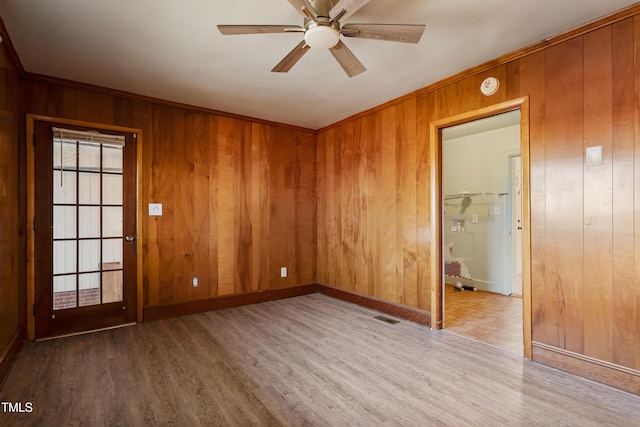 unfurnished room featuring hardwood / wood-style flooring, ceiling fan, wood walls, and ornamental molding