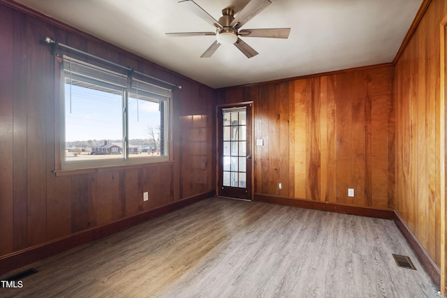 empty room featuring wooden walls, ceiling fan, and light wood-type flooring