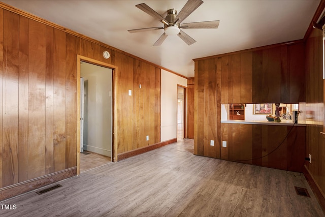 interior space featuring ceiling fan, wooden walls, light hardwood / wood-style floors, and ornamental molding