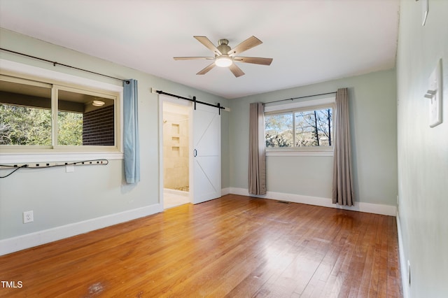 unfurnished room with a barn door, light hardwood / wood-style flooring, and ceiling fan