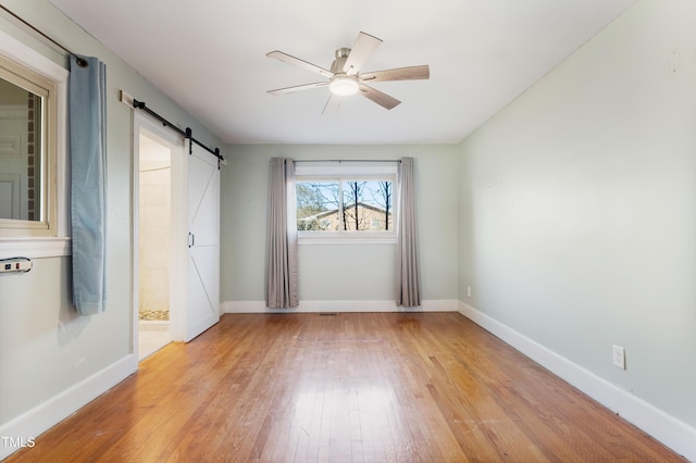 unfurnished room with ceiling fan, a barn door, and light wood-type flooring