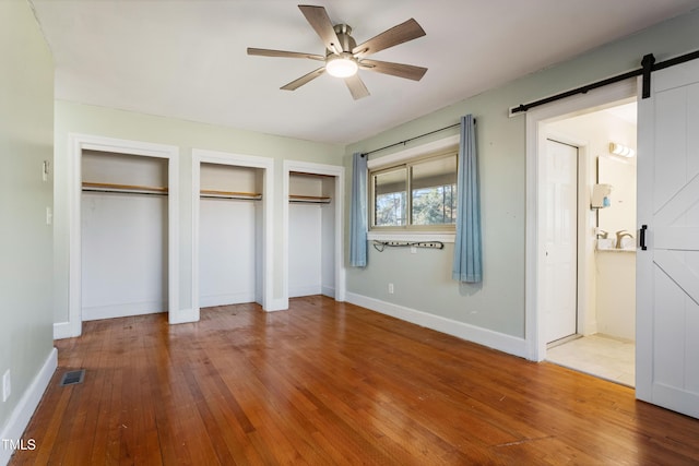 unfurnished bedroom featuring hardwood / wood-style floors, ceiling fan, a barn door, and multiple closets