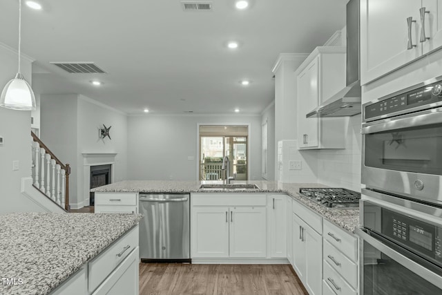 kitchen with white cabinets, wall chimney range hood, sink, ornamental molding, and appliances with stainless steel finishes