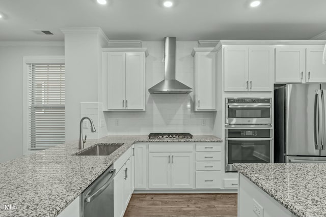 kitchen with white cabinetry, sink, wall chimney exhaust hood, appliances with stainless steel finishes, and ornamental molding