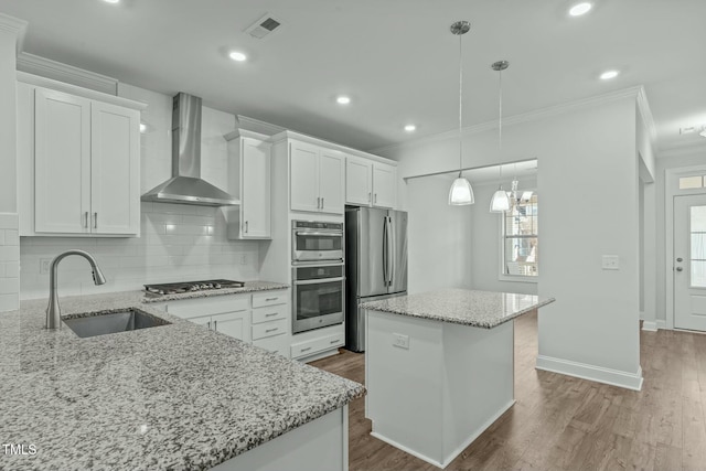 kitchen featuring white cabinetry, a center island, wall chimney exhaust hood, sink, and appliances with stainless steel finishes