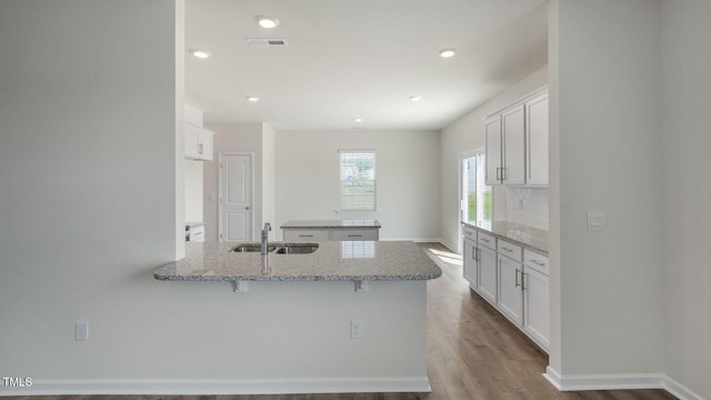 kitchen featuring kitchen peninsula, light stone countertops, light wood-type flooring, sink, and white cabinets