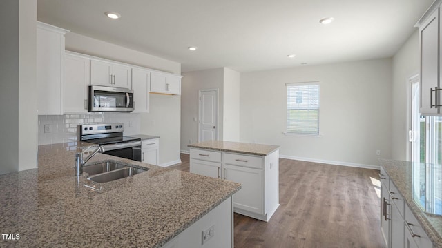 kitchen with sink, light stone countertops, a kitchen island, white cabinetry, and stainless steel appliances