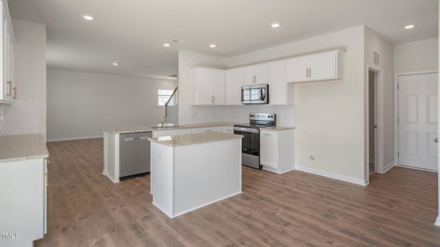 kitchen with white cabinets, appliances with stainless steel finishes, a center island, and hardwood / wood-style flooring