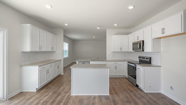 kitchen with hardwood / wood-style floors, white cabinets, light stone countertops, a kitchen island, and stainless steel appliances