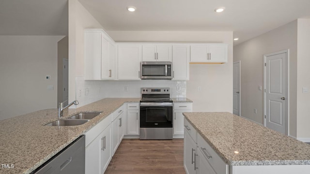 kitchen with light stone countertops, appliances with stainless steel finishes, sink, white cabinets, and hardwood / wood-style floors