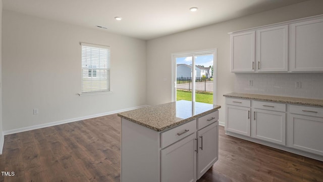 kitchen with light stone countertops, dark hardwood / wood-style flooring, backsplash, a kitchen island, and white cabinetry