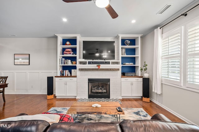 living room featuring built in shelves, ceiling fan, a fireplace, and light hardwood / wood-style floors