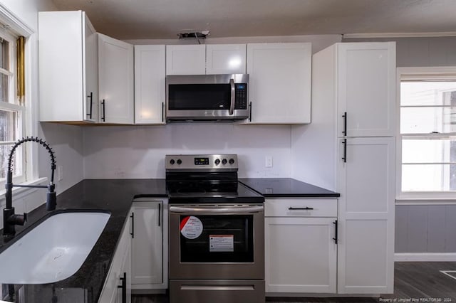 kitchen with dark hardwood / wood-style flooring, stainless steel appliances, sink, dark stone countertops, and white cabinets