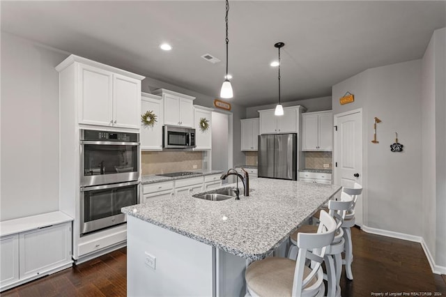 kitchen featuring appliances with stainless steel finishes, a kitchen island with sink, dark wood-type flooring, sink, and white cabinetry