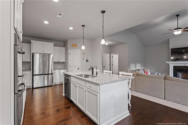 kitchen with white cabinetry, sink, stainless steel appliances, light stone counters, and a kitchen island with sink