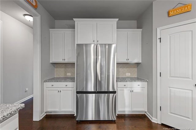 kitchen with white cabinets, dark hardwood / wood-style floors, tasteful backsplash, light stone counters, and stainless steel refrigerator