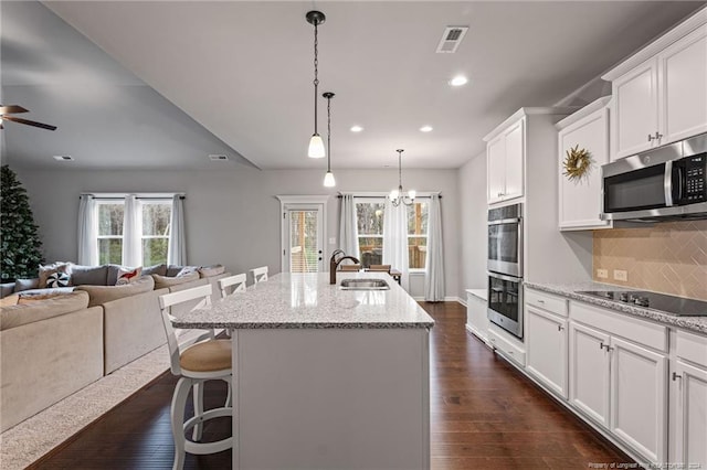 kitchen featuring white cabinetry, stainless steel appliances, a kitchen breakfast bar, dark hardwood / wood-style flooring, and an island with sink