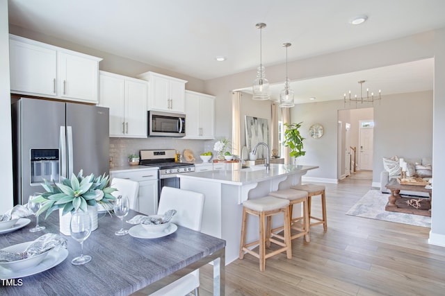 kitchen featuring appliances with stainless steel finishes, light wood-type flooring, a kitchen island with sink, pendant lighting, and white cabinetry