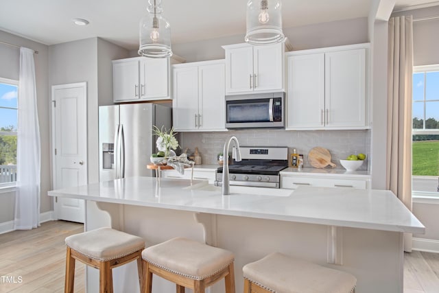 kitchen with a center island with sink, light wood-type flooring, white cabinetry, and appliances with stainless steel finishes