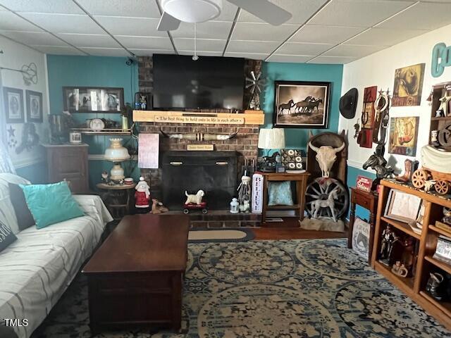 living room with ceiling fan, a fireplace, and a drop ceiling