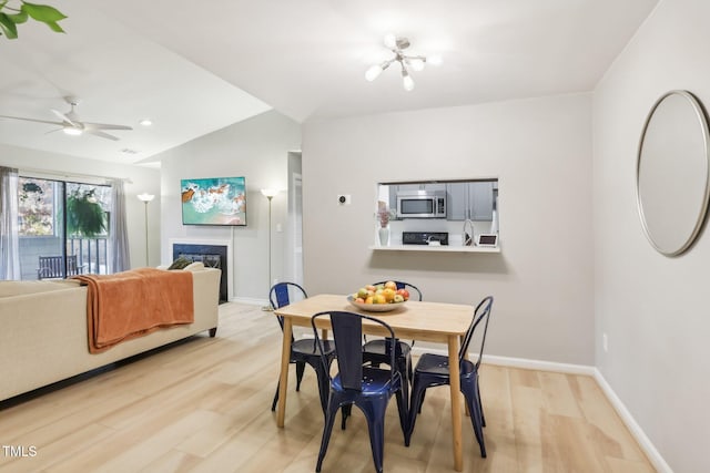 dining space featuring lofted ceiling, a fireplace, ceiling fan with notable chandelier, and light hardwood / wood-style flooring