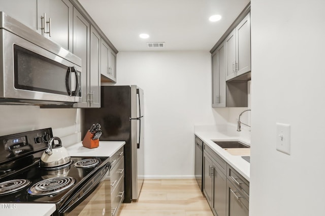 kitchen with gray cabinets, light hardwood / wood-style floors, sink, and appliances with stainless steel finishes