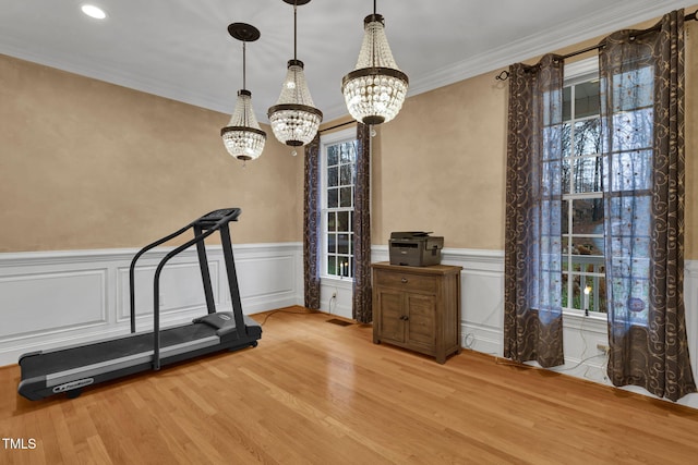 exercise room featuring a notable chandelier, light wood-type flooring, ornamental molding, and a wealth of natural light