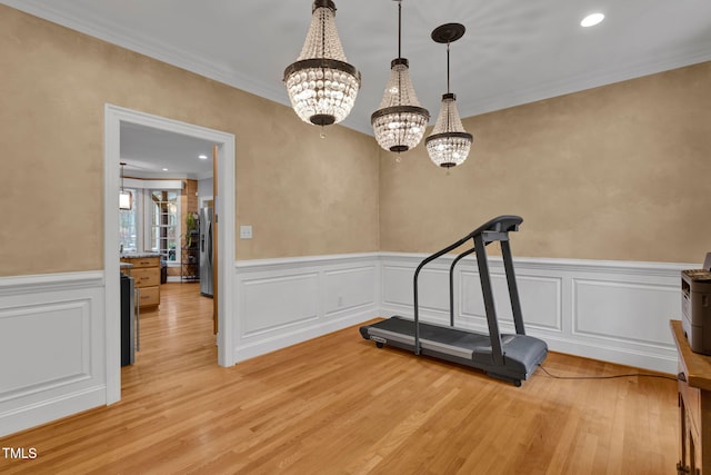 exercise room featuring light wood-type flooring, an inviting chandelier, and crown molding